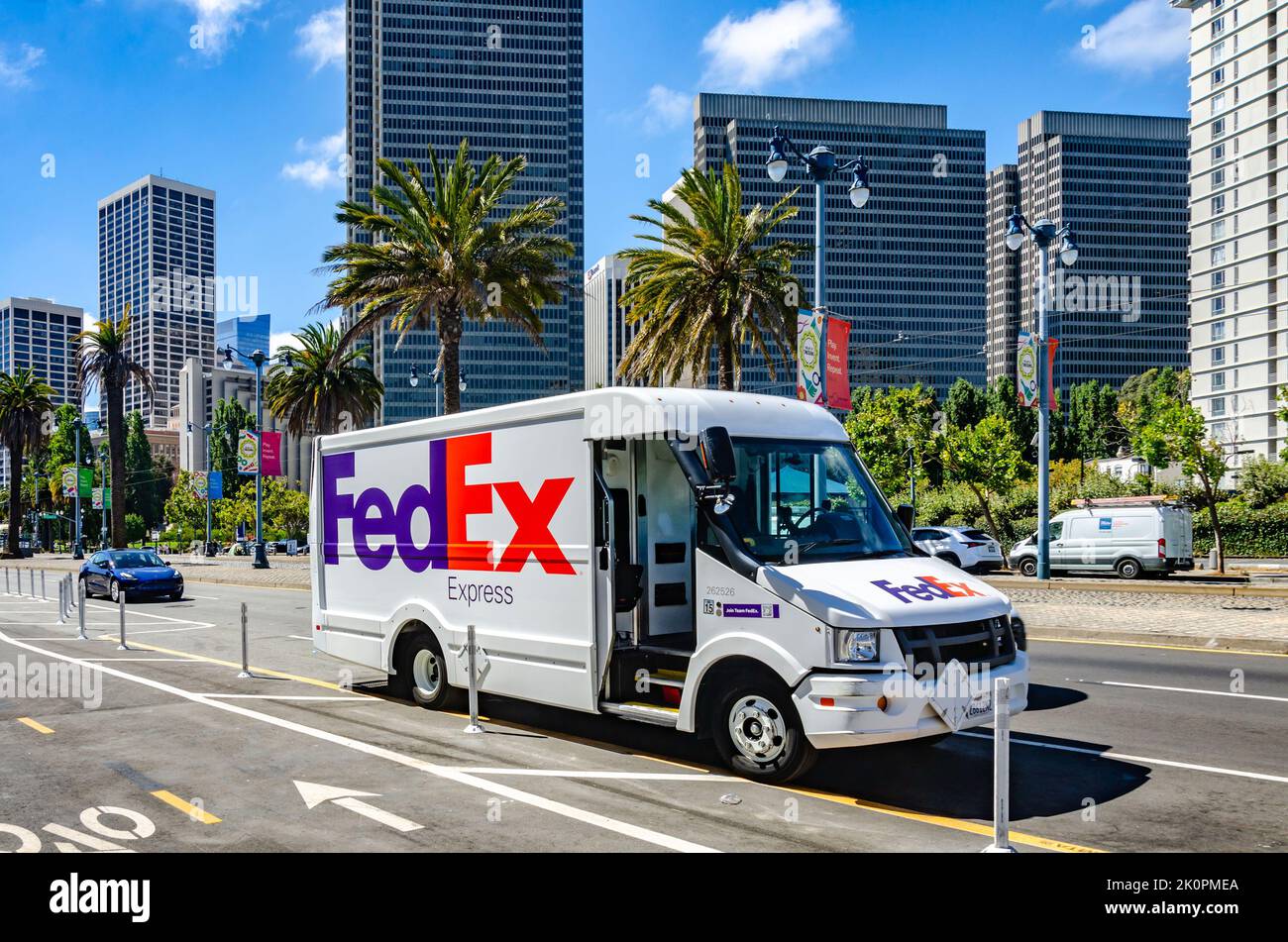 A white FedEx courier delivery van on The Embarcadero in San Francisco, California in front of tall tower blocks and palm trees. Stock Photo