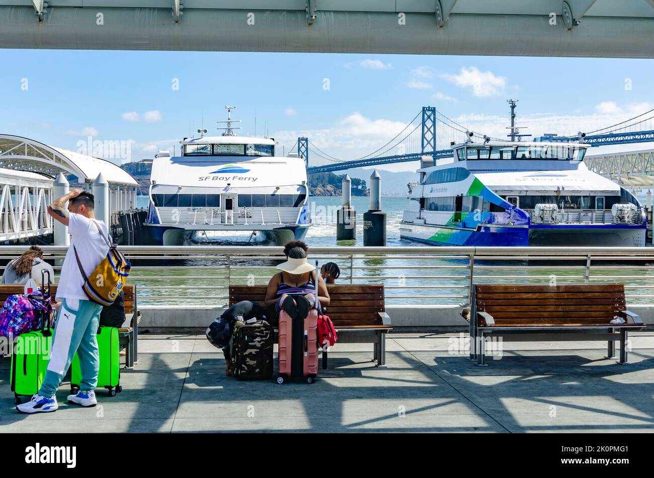 Two San Francisco Bay Ferries moored in the San Francisco Ferry Terminal. Passengers sit and wait on wooden benches. Stock Photo