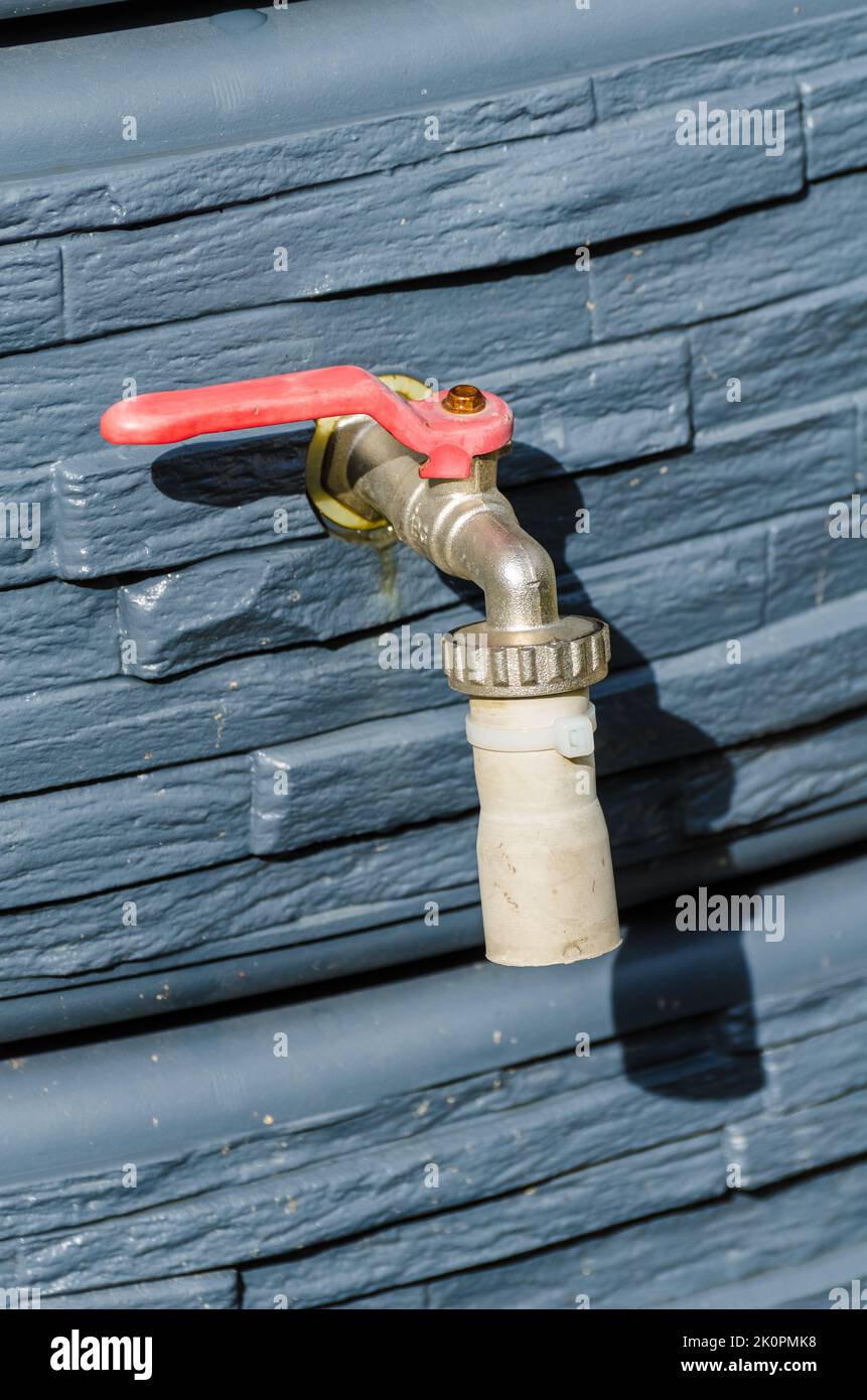 Faucet with red handle of a rain barrel in a garden for water supply Stock Photo