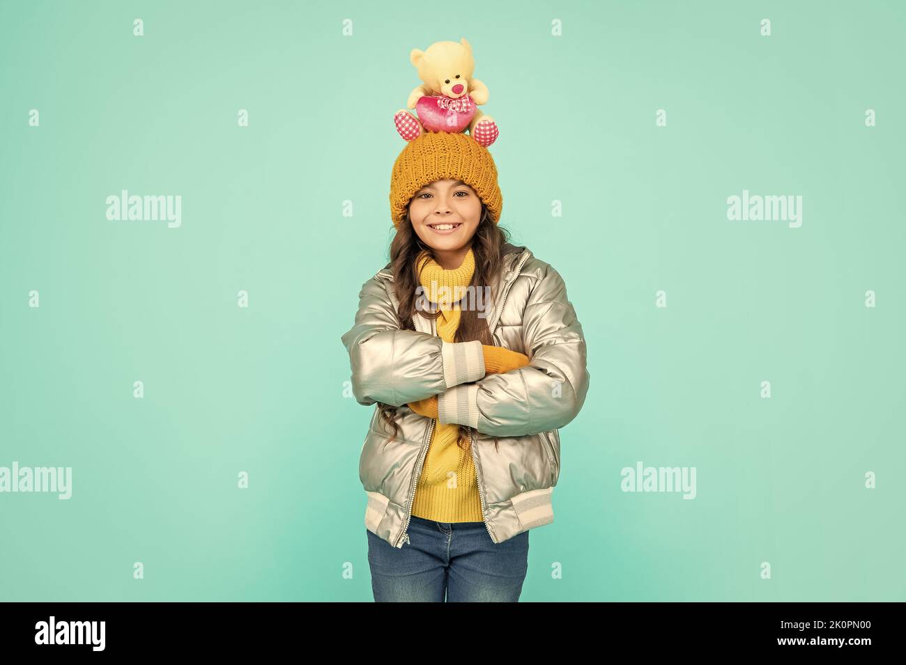 happy teen girl with toy bear crossed hands. child wear warm clothes on blue background. Stock Photo