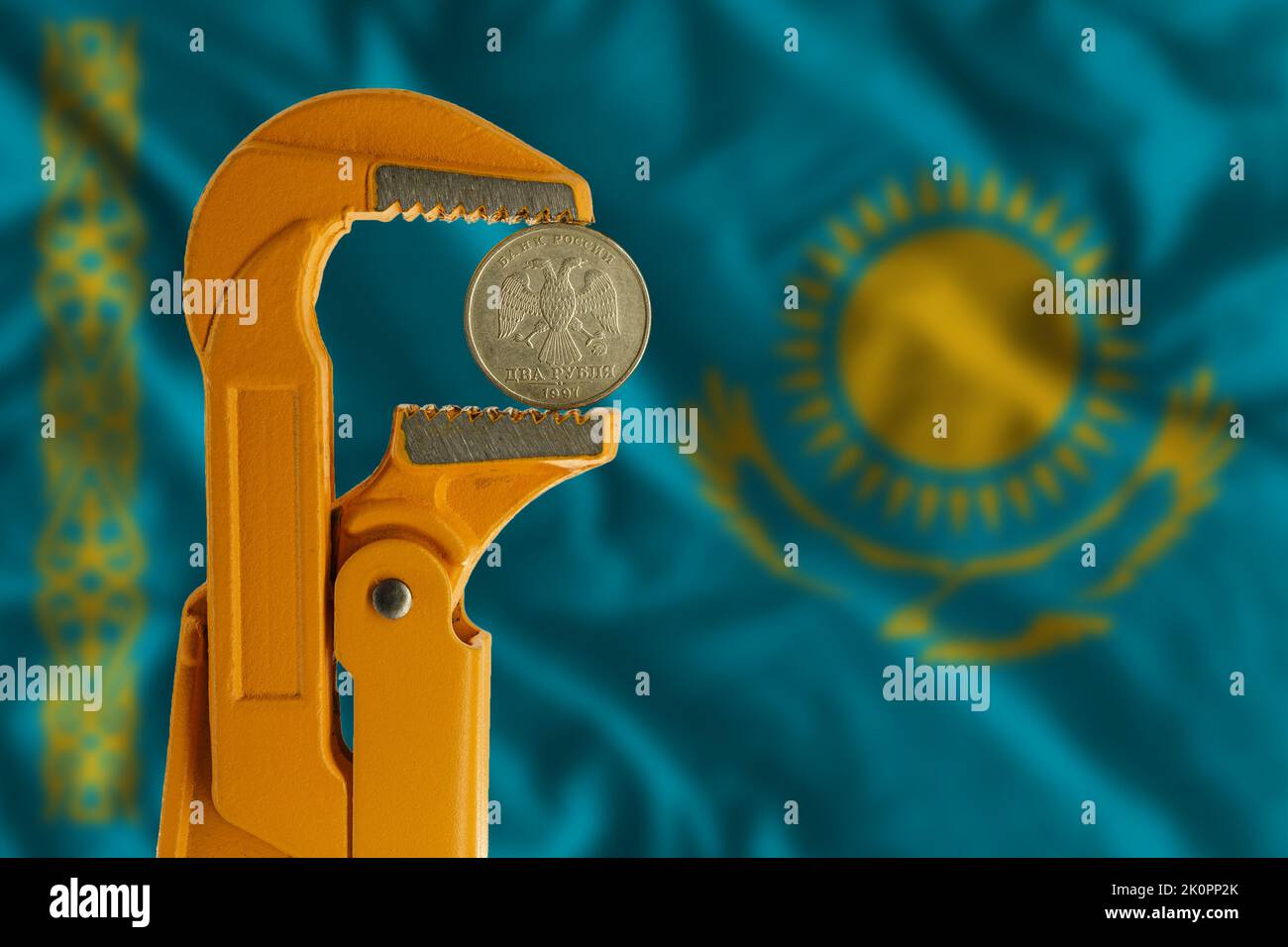 Russian two rubles coin held in an orange plumber wrench on the background of the flag of Kazakhstan. Reverse side Stock Photo