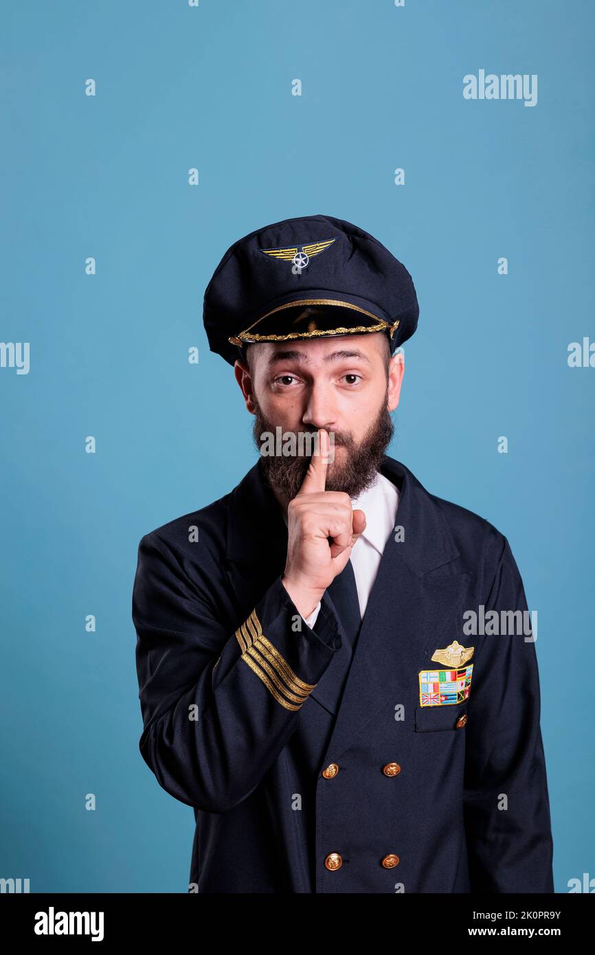 Portrait of captain showing silent gesture, looking at camera with forefinger on lips. Aviation academy plane pilor front view, airforce aviator keeping secret, quiet, silence sign Stock Photo