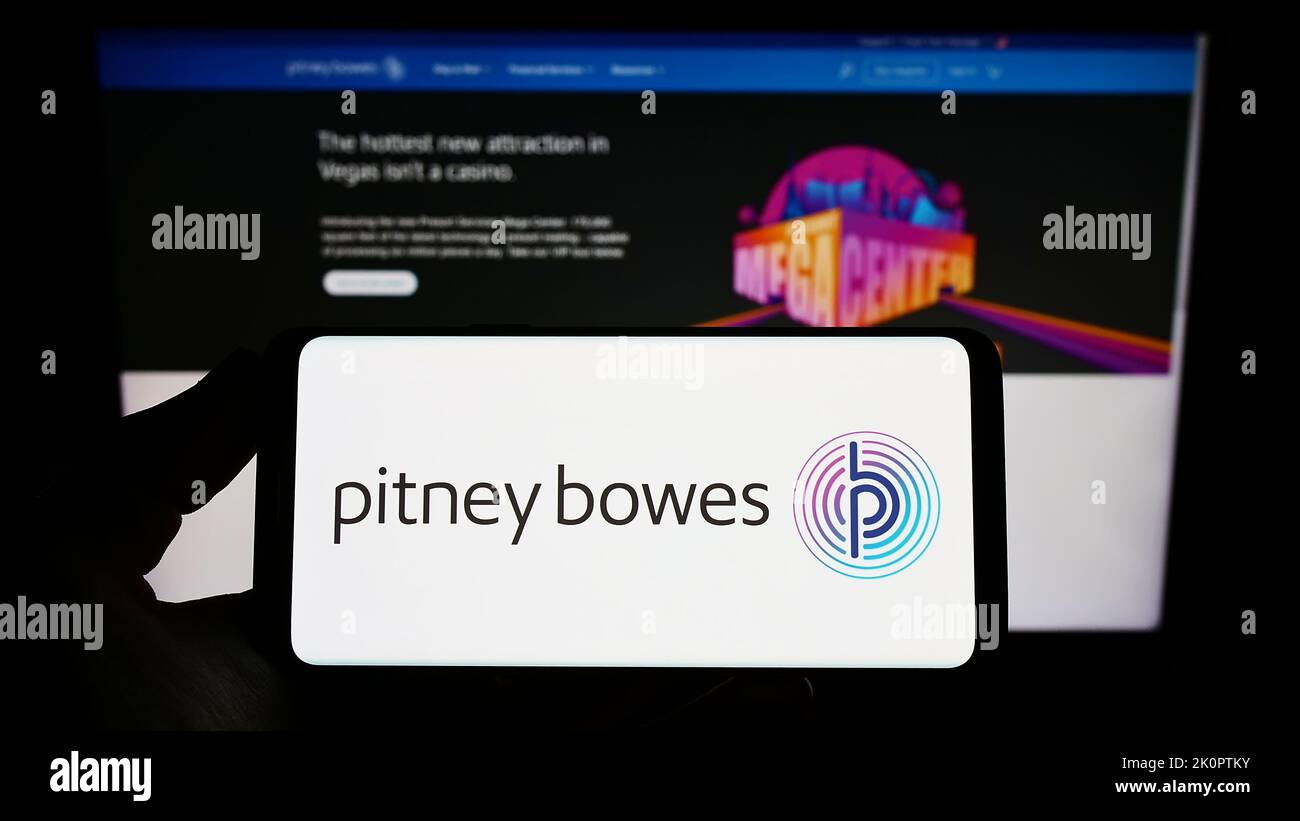 Person holding smartphone with logo of US technology company Pitney Bowes Inc. on screen in front of website. Focus on phone display. Stock Photo