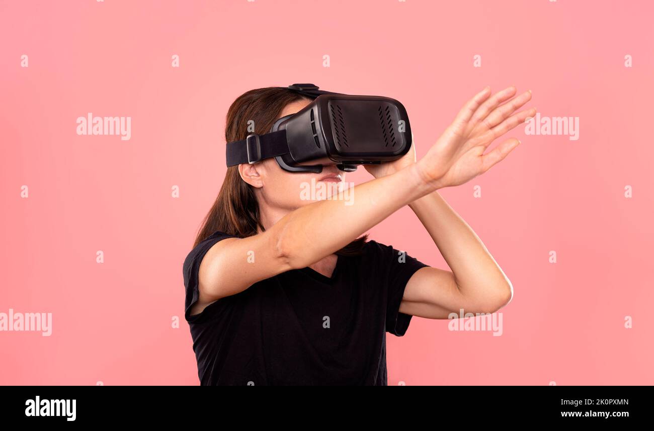Woman wearing a virtual reality headset, pink background. Stock Photo