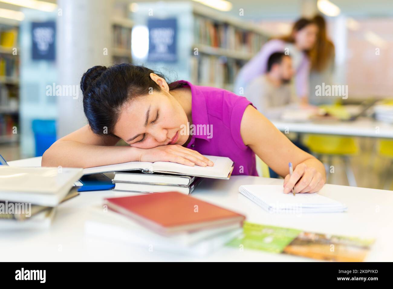 Tired Asian woman sleeping on stack of books in library Stock Photo - Alamy