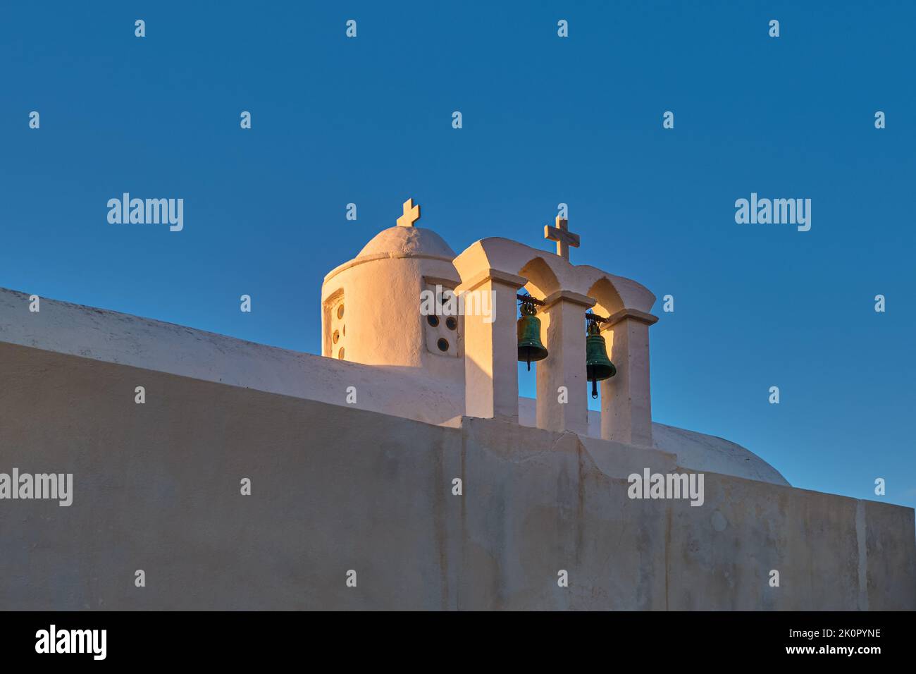 Whitewashed Greek Orthodox chapel, small belfry with cross and bell, roof and dome at sunset sky background. Close-up shot. Milos island, Greece Stock Photo