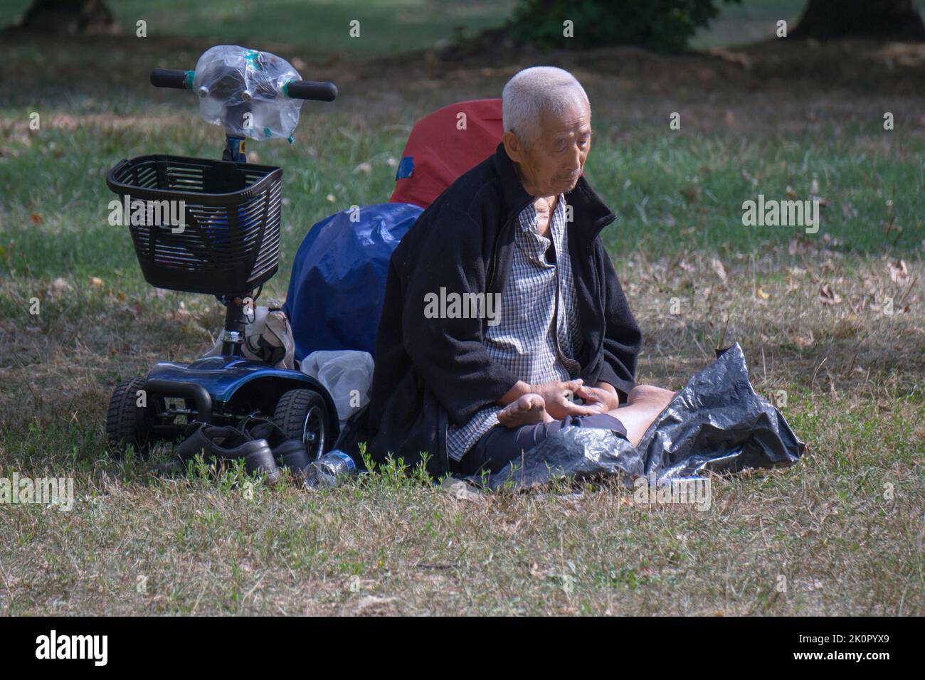 A seated 87 year old man does Falun Gong slow-moving exercises. In a park in Queens, New York, a very diverse place. Stock Photo
