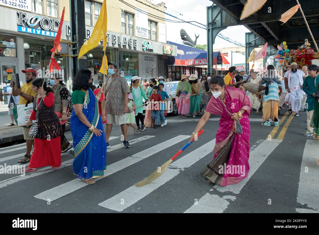 A Hindu woman sweeping a path where deities will pass. Under the elevated subway during the Ratha Yatra parade in Ozone Park, Queens, New York. Stock Photo