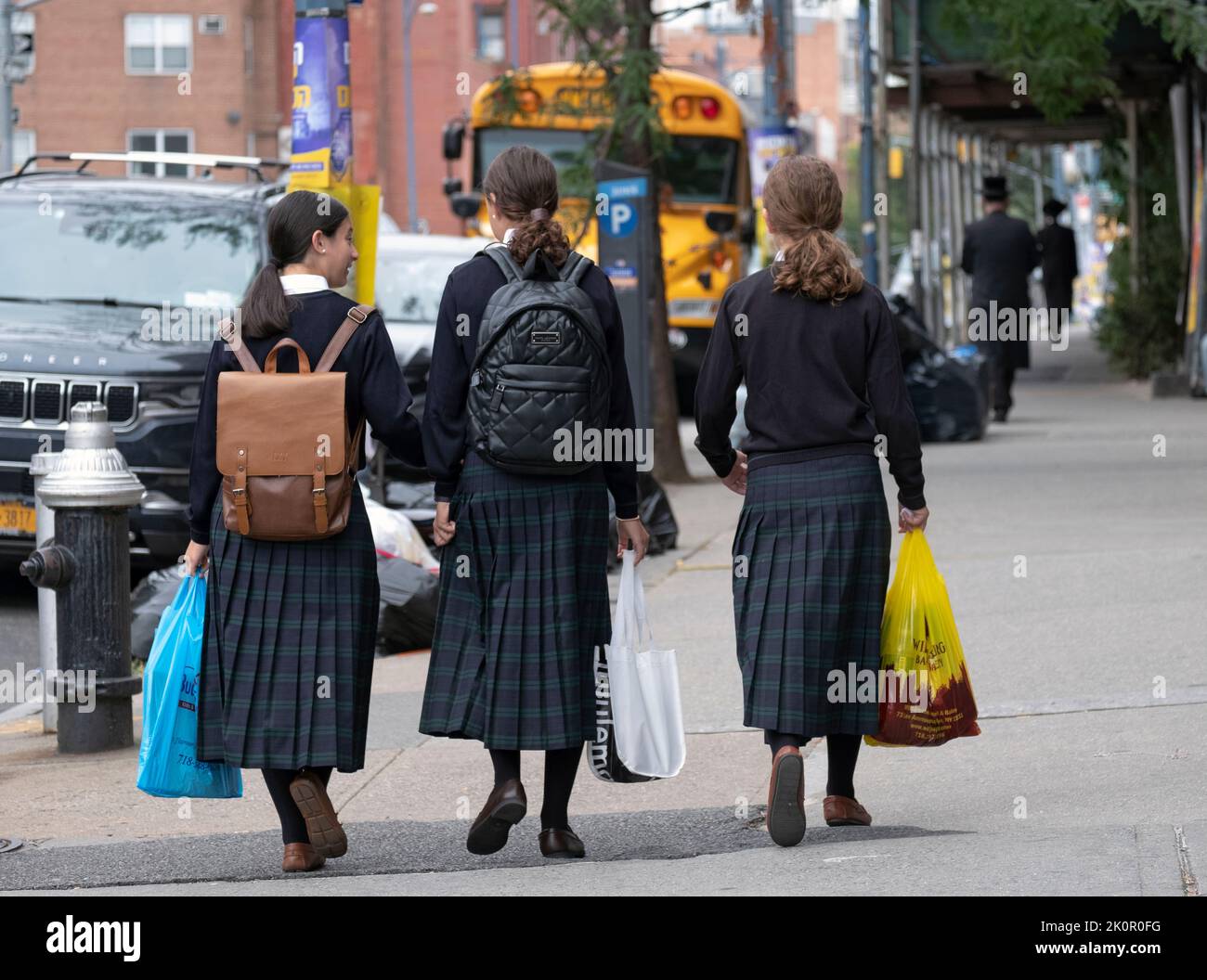 3 modestly clothed orthodox Jewish girls dressed almost identically, walk to school on Lee Ave. in Williamsburg, Brooklyn, New York City. Stock Photo