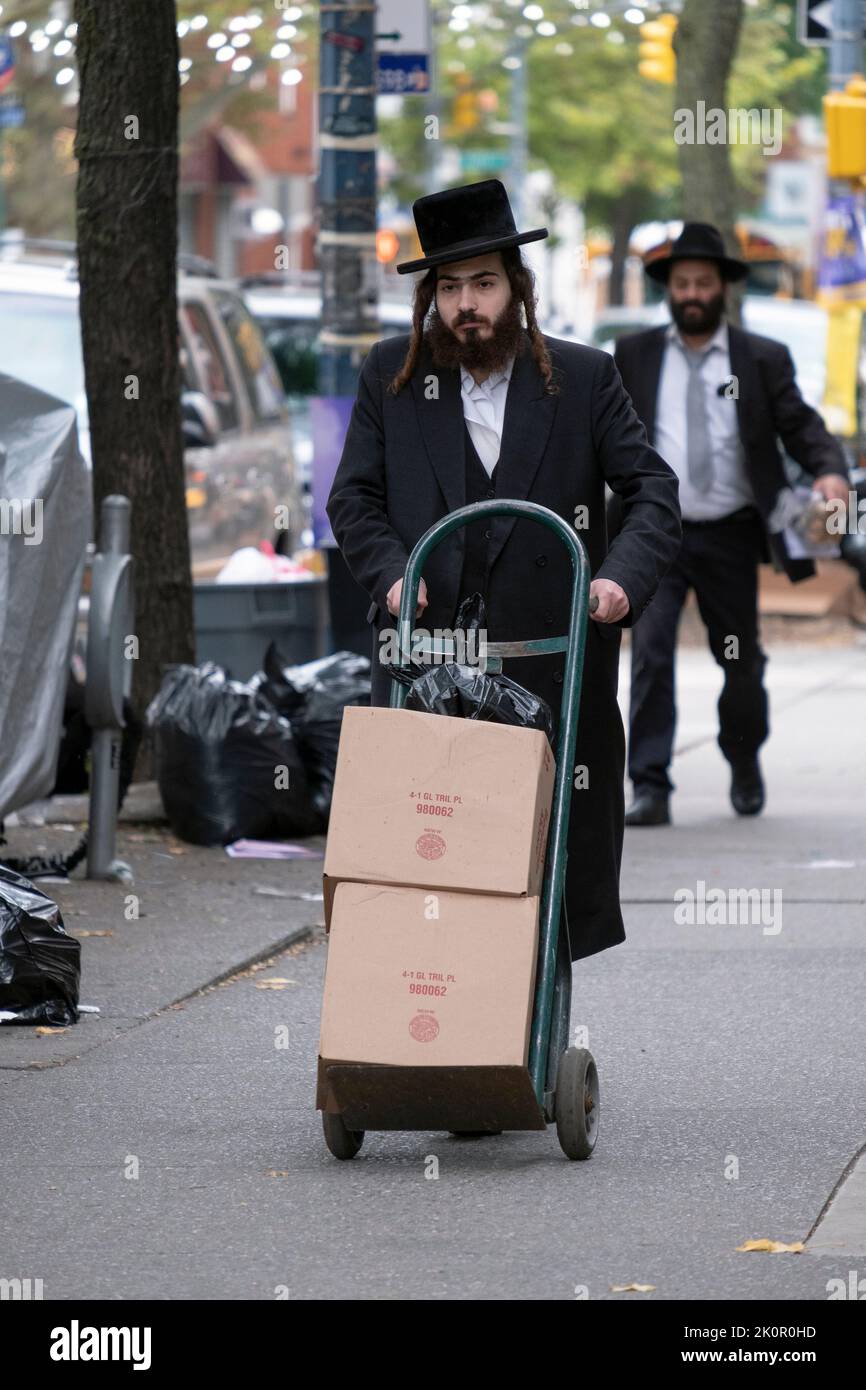 An orthodox Jewish man using a hand truck brings cans of paint from a hardware store to his car. On Lee Ave. in Williamsburg, Brooklyn, New York. Stock Photo