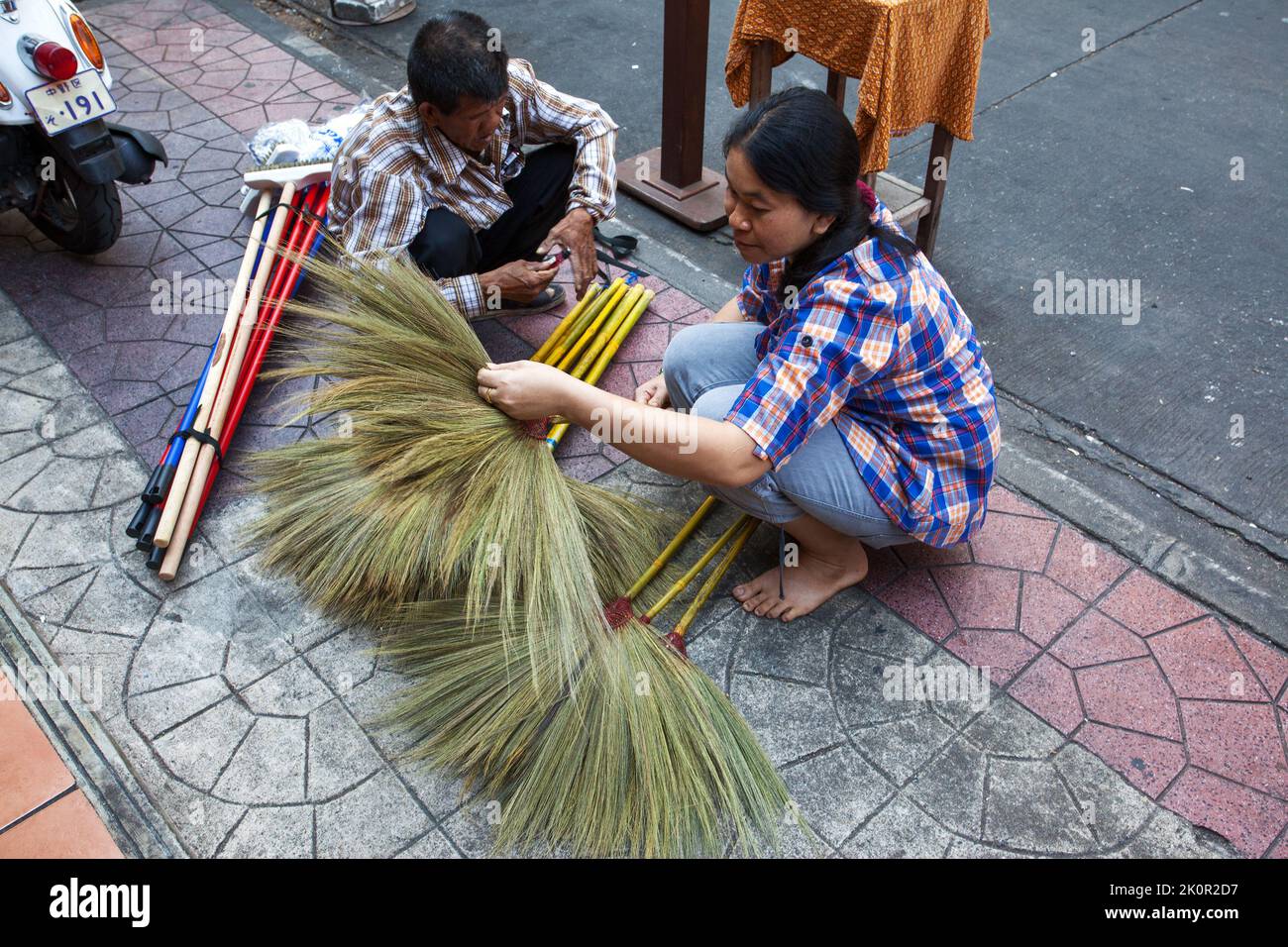 Bangkok, Thailand - December 12, 2011: Street vendor of brooms with buyer on the sidewalk in Bangkok. Evaluation of quality Stock Photo