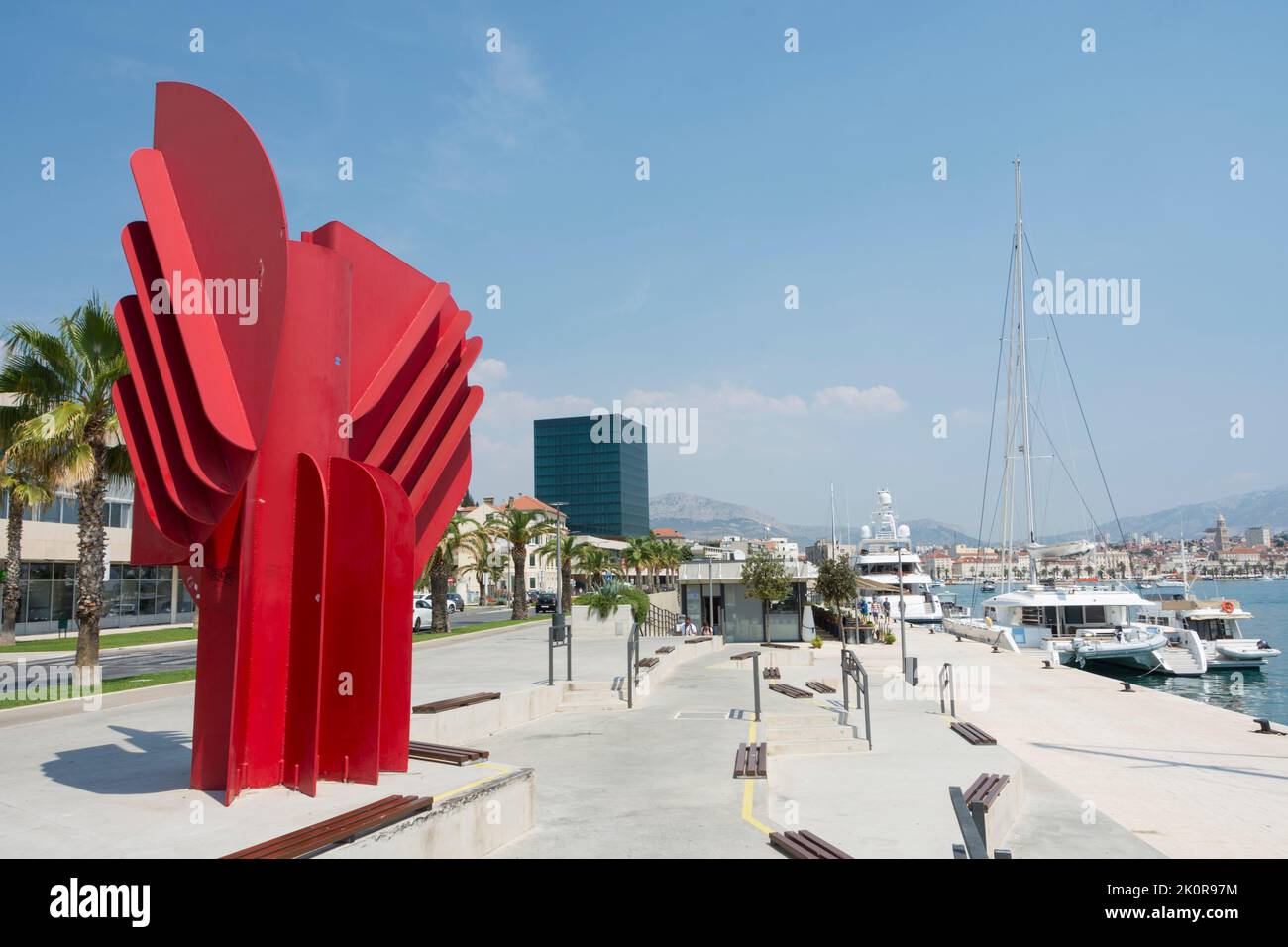 Red sculpture of visual artist Jagoda Buic and glass cube of Hotel Marjan in the background on the boulevard of the ACI Marina in Split, Croatia Stock Photo
