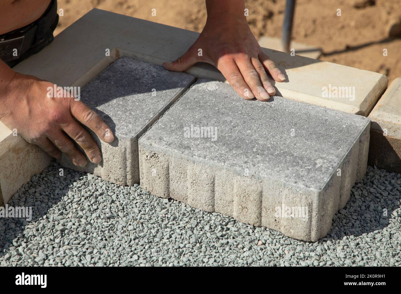 A gloved craftsman lays down the paving stones in layers. Laying gray