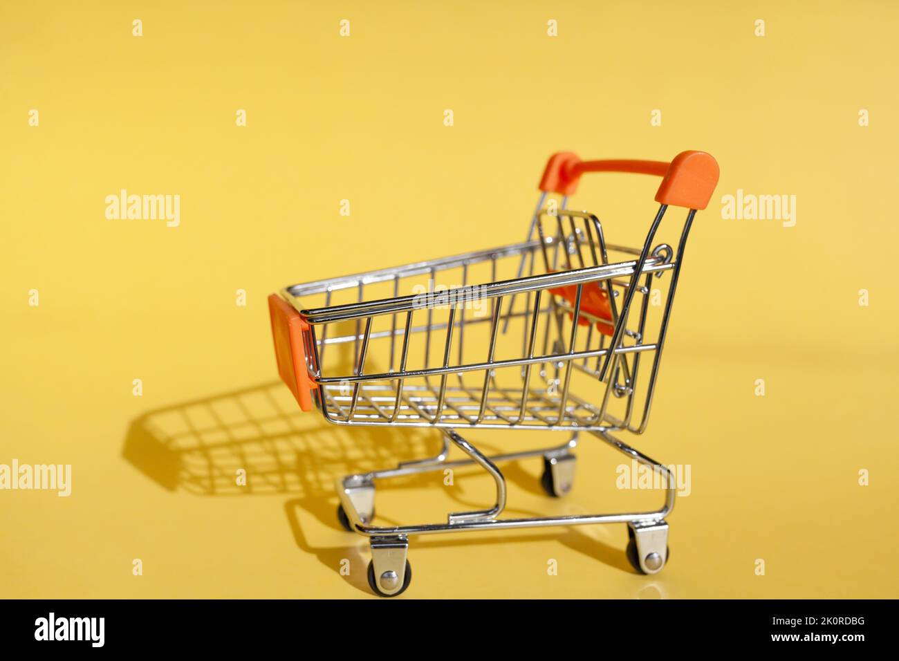 Small supermarket grocery push cart for shopping. Shopaholic. Buyer. Shopping concept. Close-up. Isolated shopping trolley on a yellow background. Cop Stock Photo