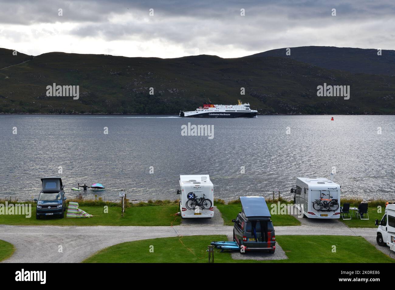 The Caledonian MacBrayne ferry leaving Ullapool bound for Stornoway in the outer Hebrides with campervans on the shoreline of Loch Broom. Stock Photo
