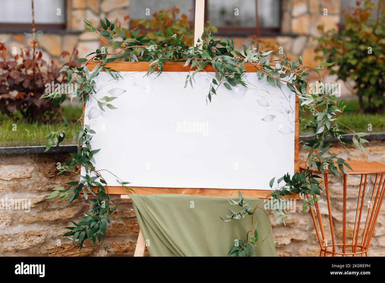 Wedding wooden board, mockup, invitation easel, with white space for an inscription, decorated with fresh greenery and green cloth. Wedding frame outd Stock Photo