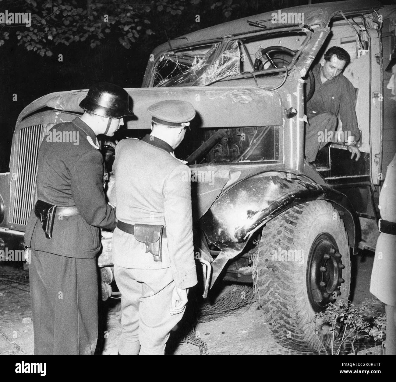 East German police (foreground) inspect a truck used to ram the Berlin wall in an escape effort from the Soviet sector of the city. Although the truck did not leave the Communist sector, the occupants were successful in escaping to the West through the hole made by the truck, Berlin, East Germany, 1961. (Photo by United States Information Agency) Stock Photo