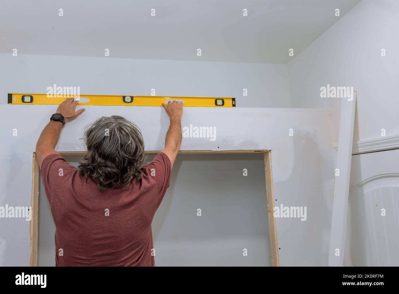 An employee checks the level of drywall before painting it using a level to ensure that the walls are equal Stock Photo