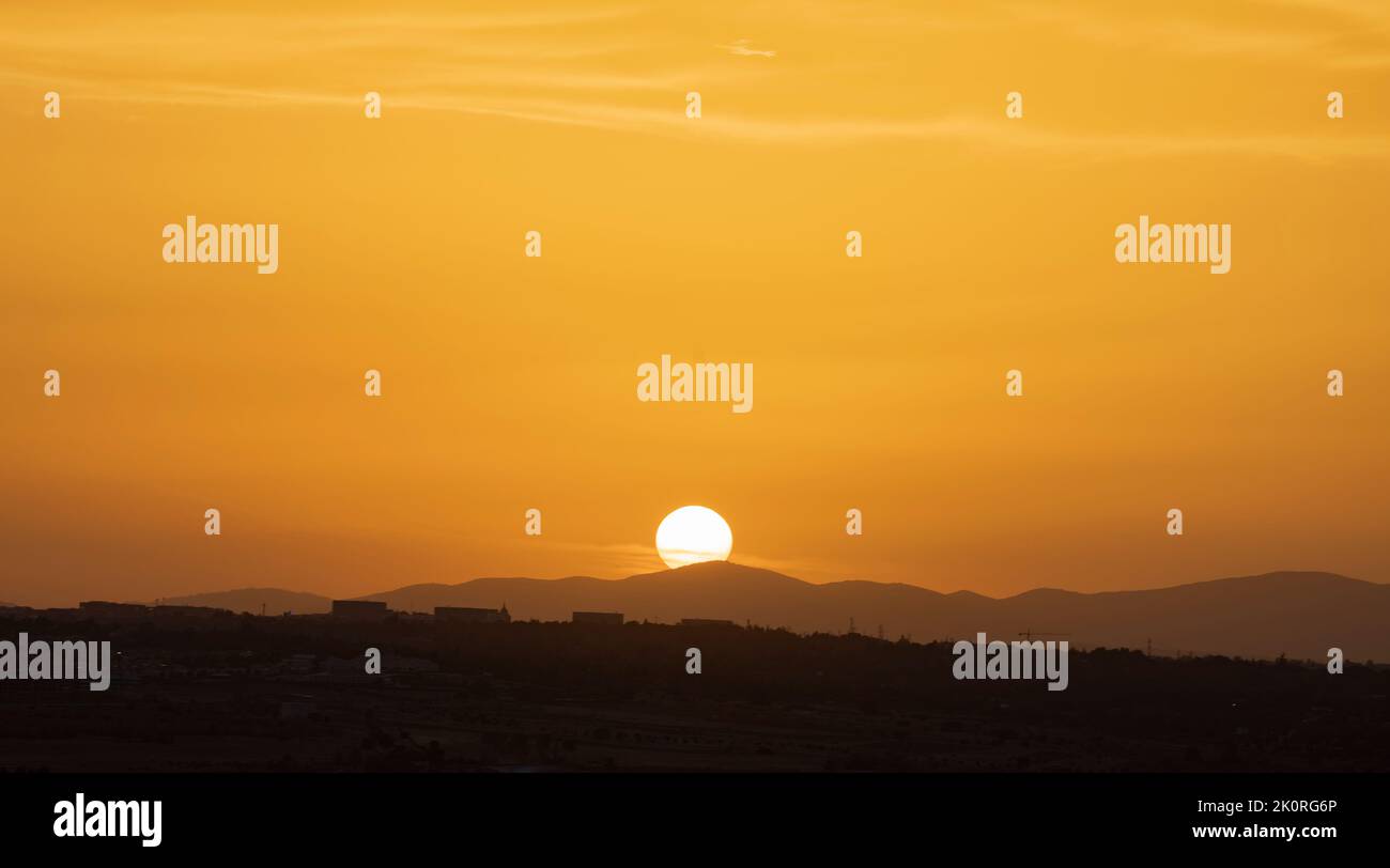 Big sun on sunset hiding behind mountains. Golden coloured sky. Copy space Stock Photo