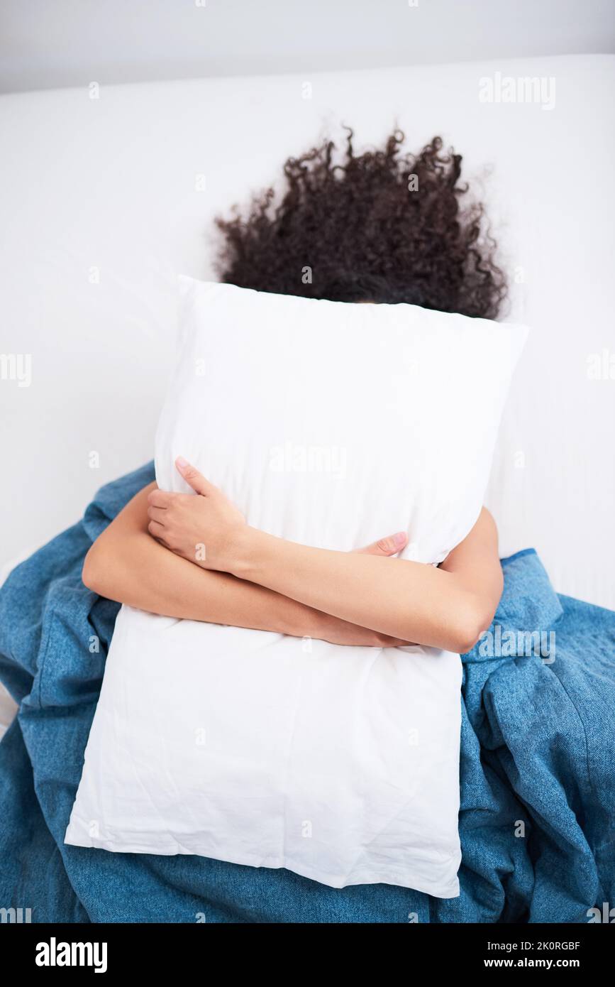 A young unidentified woman hides under her pillow in the morning Stock