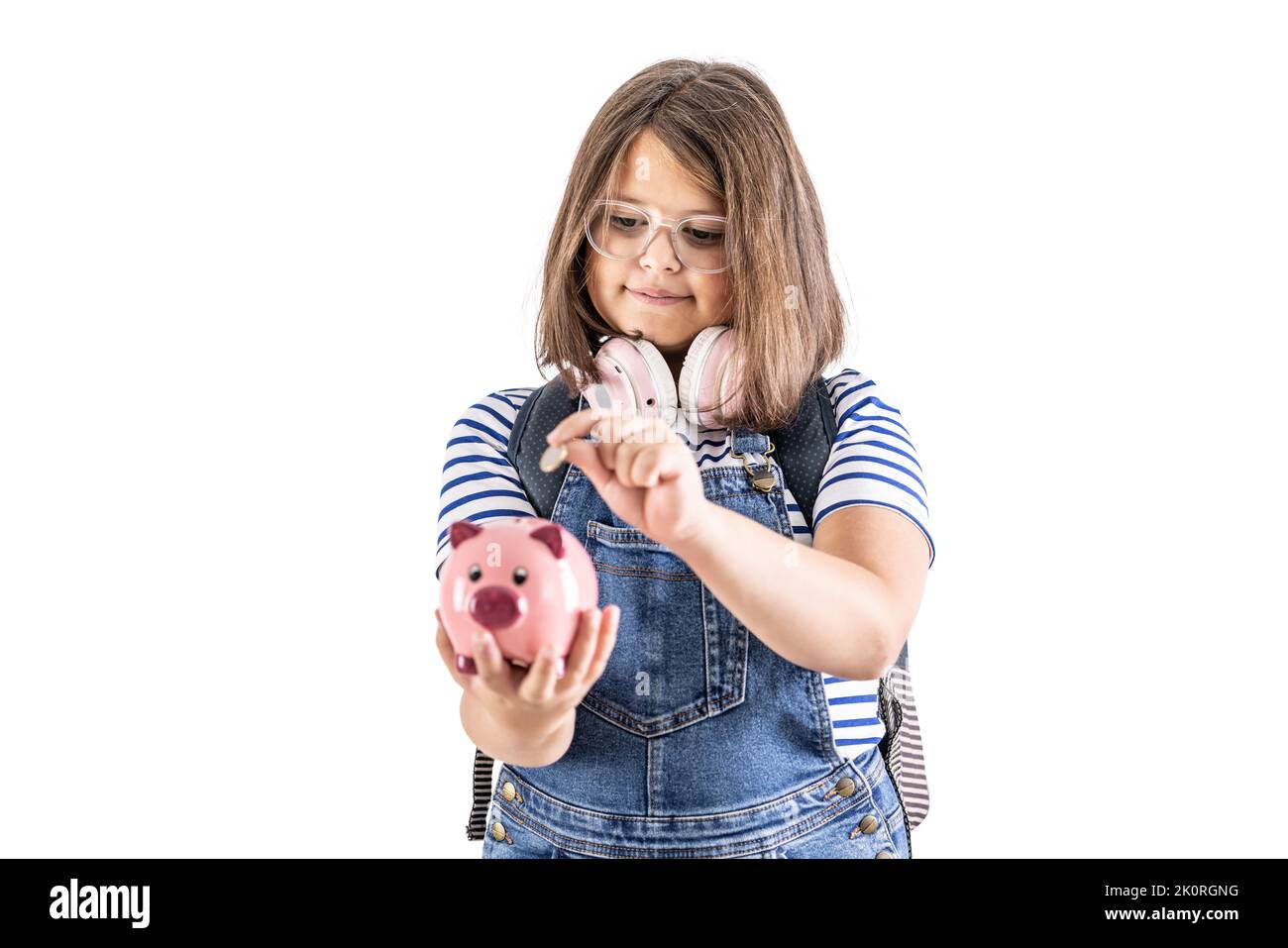 Young girl in glasses puts a coin into a piggybank. Stock Photo