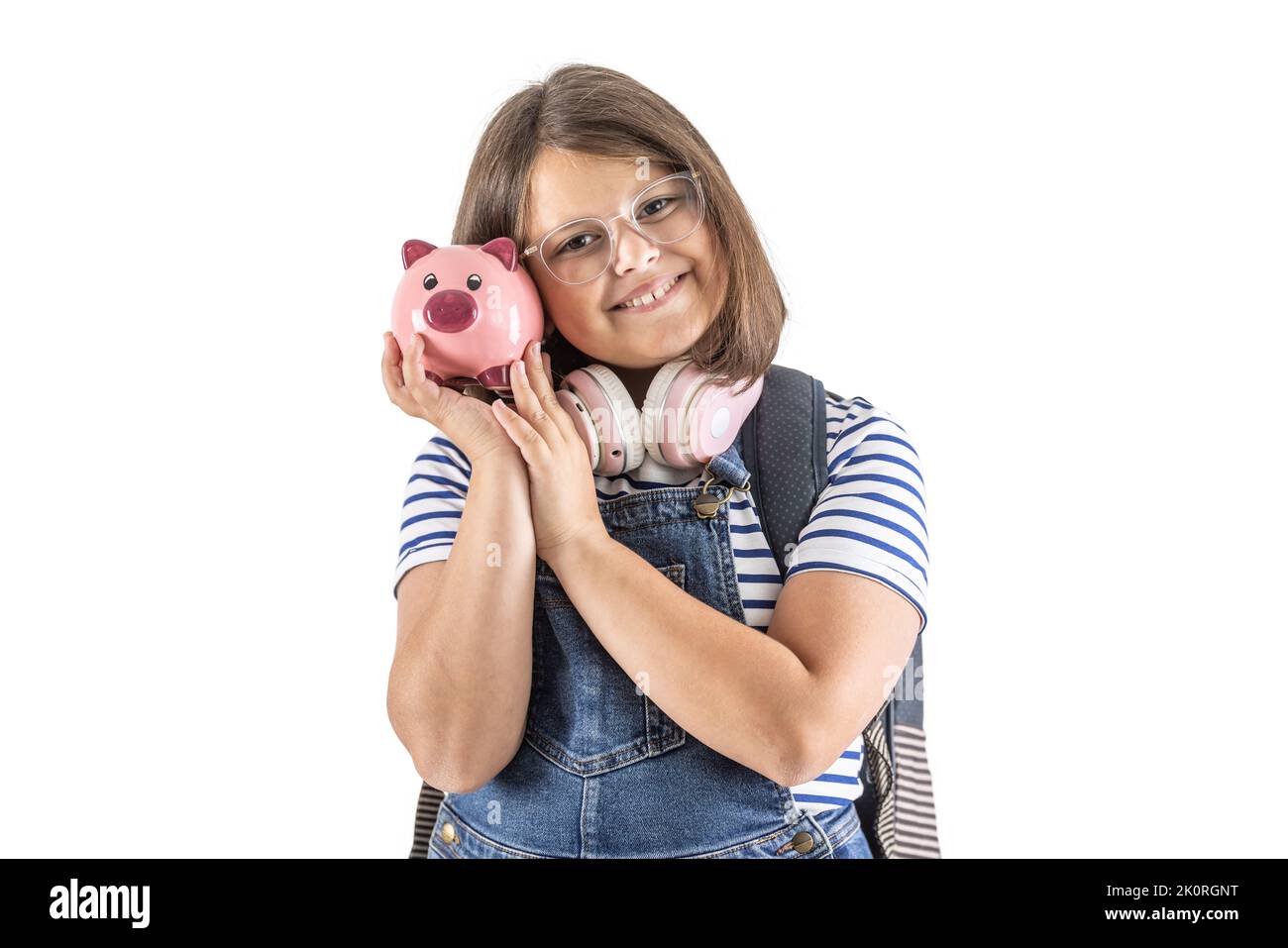 Young girl smiles as she holds her head close to a pink piggybank with savings. Stock Photo