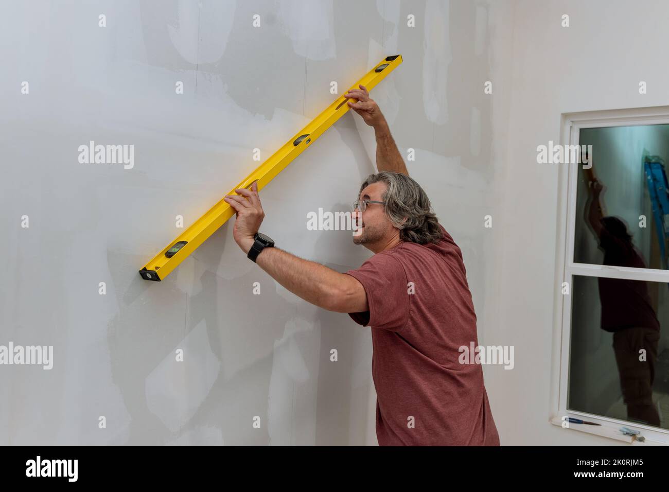 Before painting a wall of drywall, an employee makes sure that it is level by using a level Stock Photo