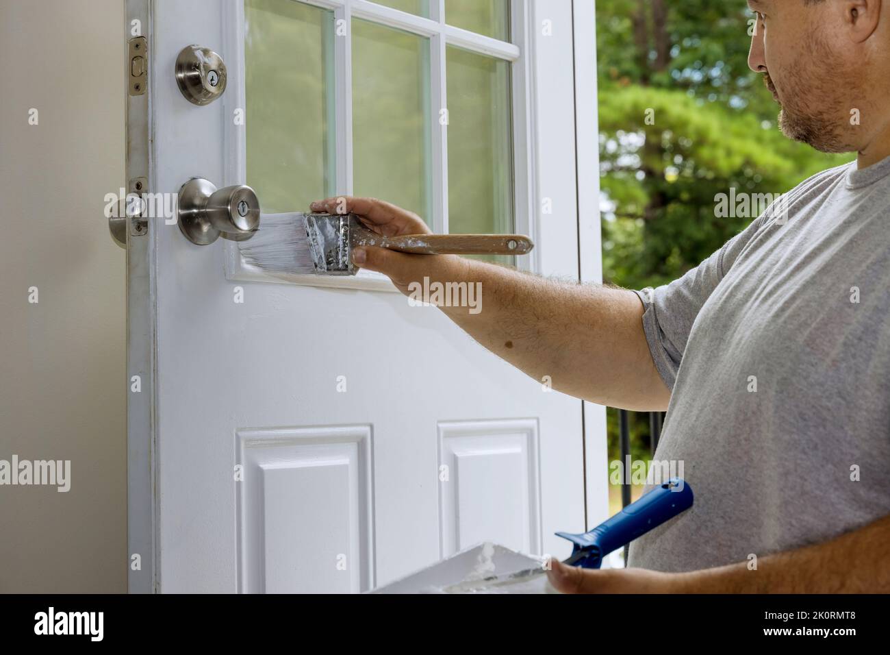 The worker painted a wooden front door with a while using a paintbrush Stock Photo