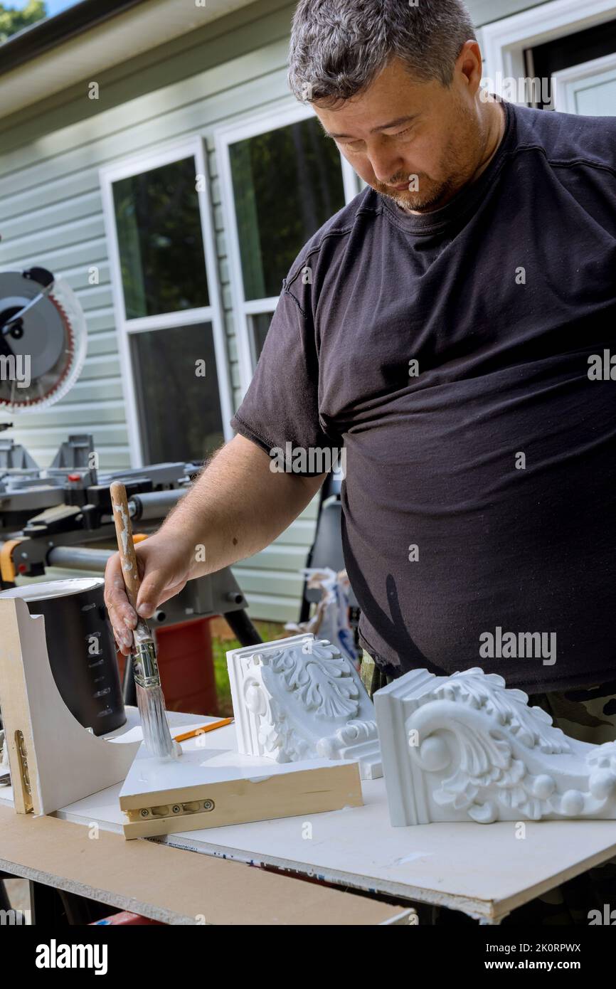 There is a worker painting wooden corbels for the kitchen island that are with the help of a paintbrush Stock Photo