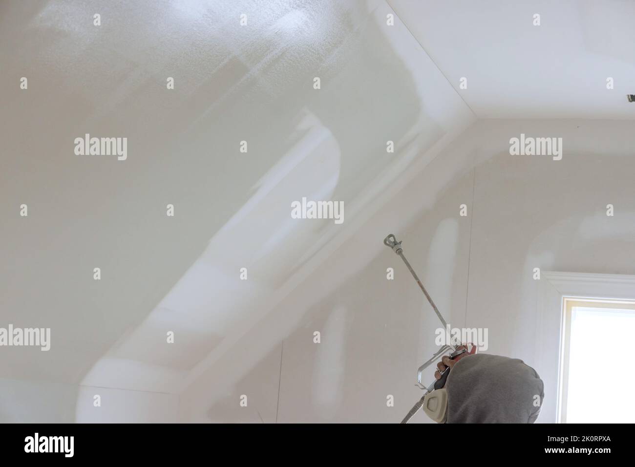 Using a spray gun and a primer, the worker paints the walls and ceilings using a spray gun that has a primer in it. Stock Photo