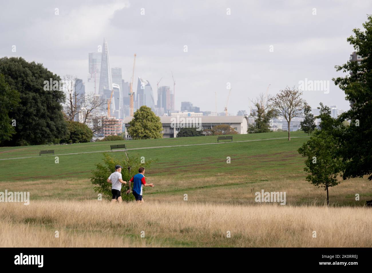 With skyscrapers in the City of London, the capital's financial district, in the distance, two runners jog across Brockwell Park in south London, on 8th September 2022, in London, England. Stock Photo