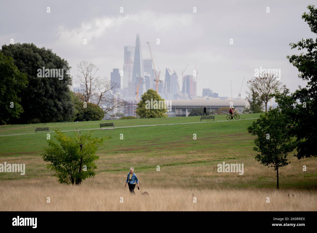 With skyscrapers in the City of London, the capital's financial district, in the distance, a a cyclist pedals uphill, a park user walks alongside and a woman walks her dog across Brockwell Park in south London, on 8th September 2022, in London, England. Stock Photo
