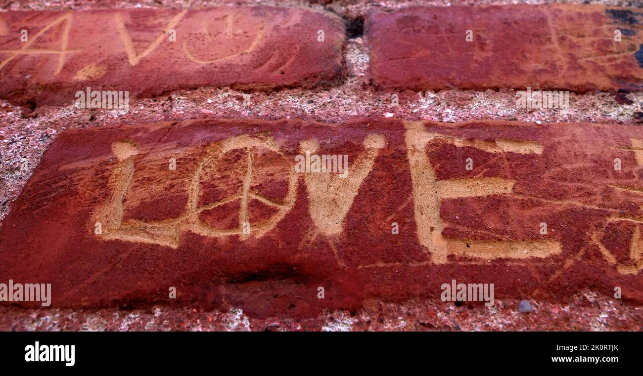 Detail of Old Red Brick Wall with Words Names and Love Scratched or Carved In Stock Photo
