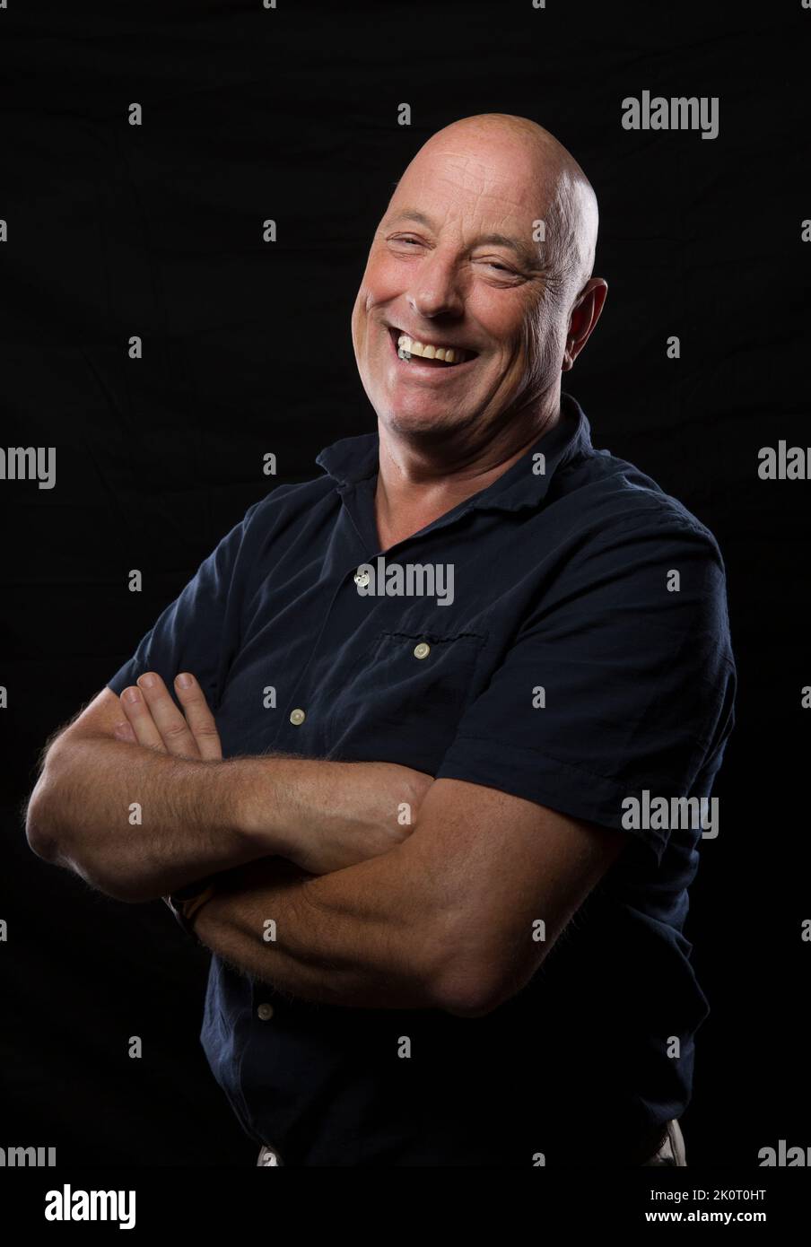 Middle aged man with arms folder and laughing into camera. Stock Photo