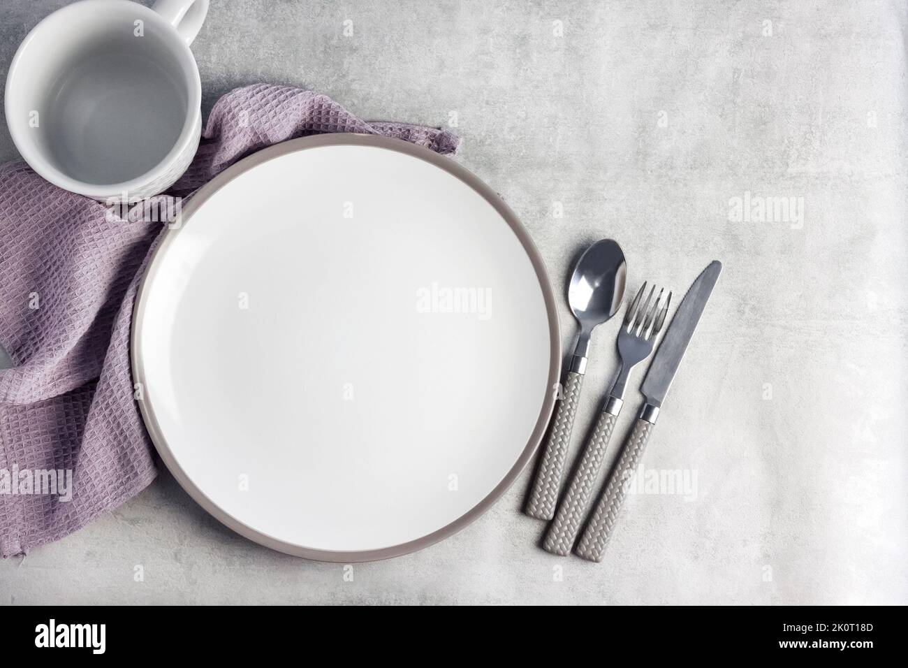 Table setting. White plate, mug, cutlery and napkin on light gray background. Flat lay, top view, copy space. Stock Photo