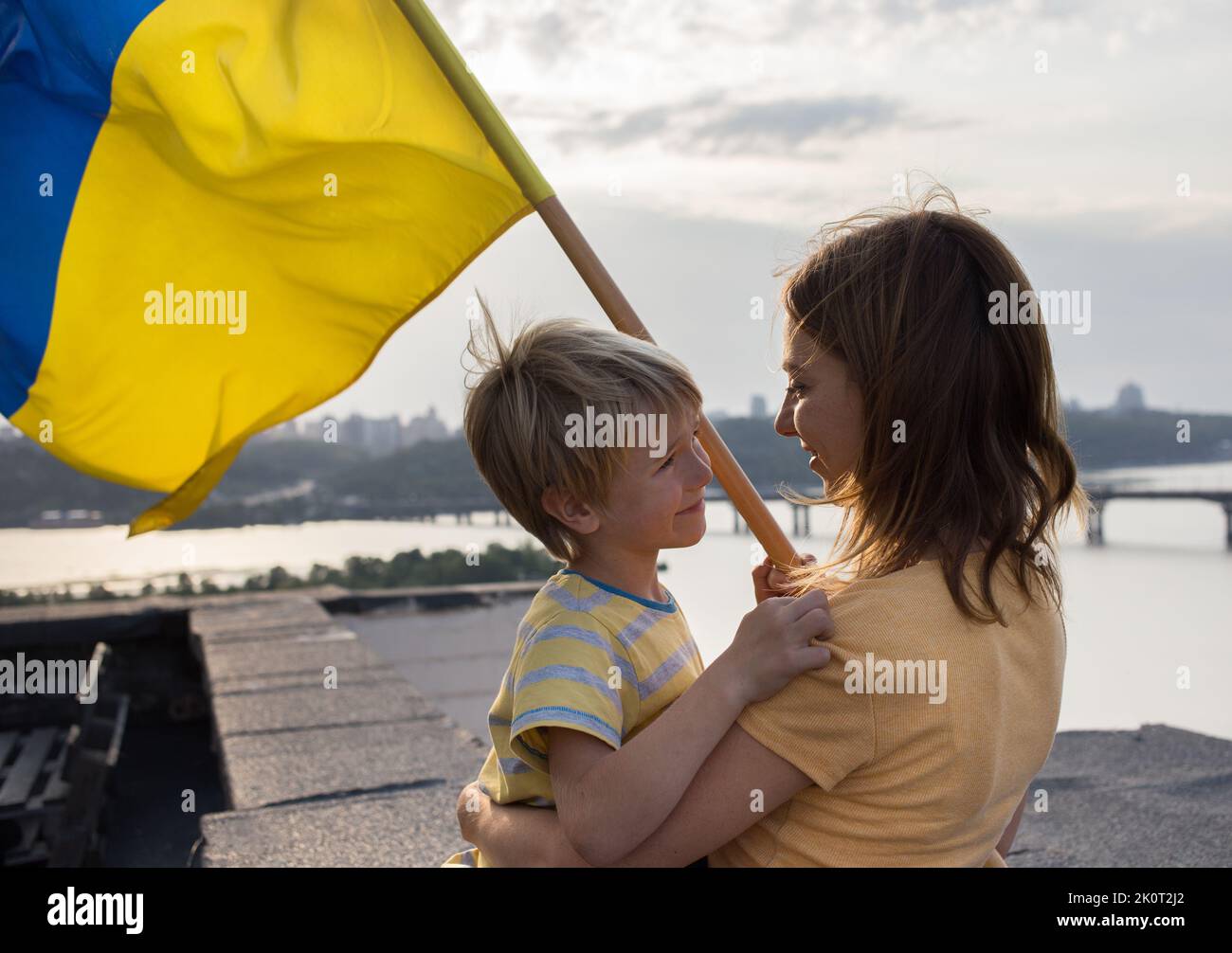 faces of a boy and a woman standing on the high roof of a house in Kyiv over the Dnieper River with a Ukrainian flag. Family, unity, support, about ea Stock Photo