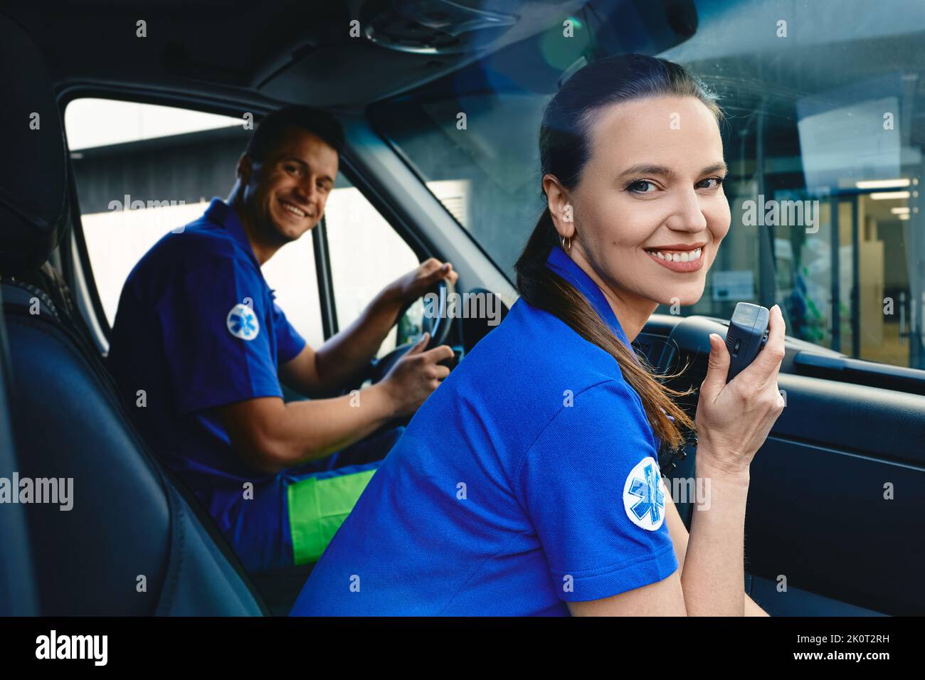 Positive female paramedic talking on portable radio while sitting in ambulance next to her emergency co-worker. Emergency medical services workers Stock Photo