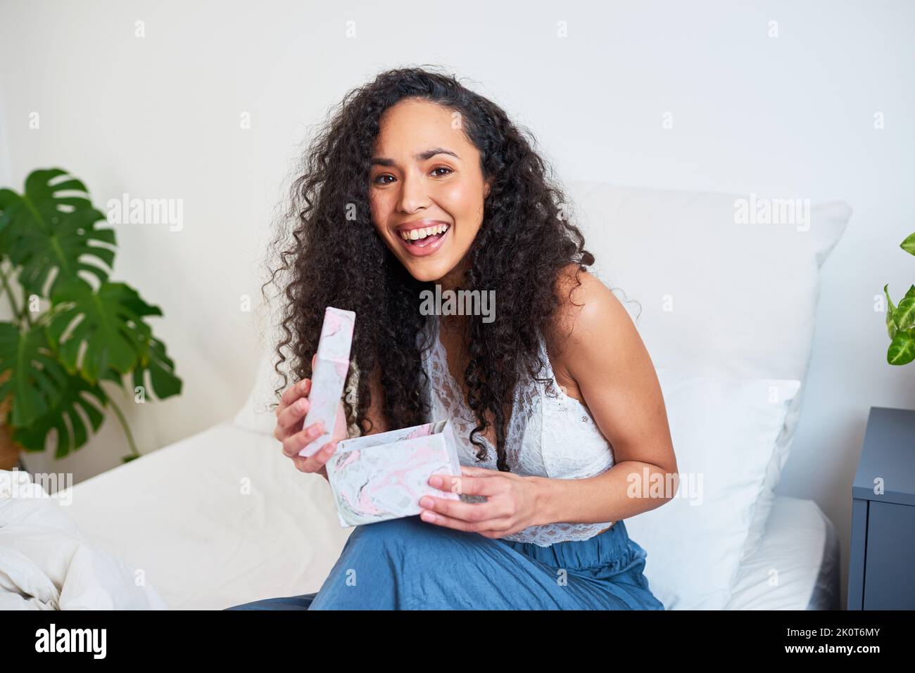 A beautiful young woman opens gift box present in bed at home Stock Photo