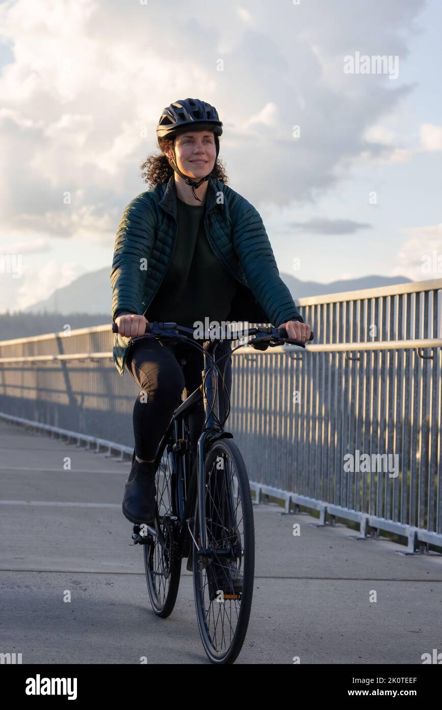 Caucasian Woman riding on a bicycle on a bike lane at Port Mann Bridge Stock Photo