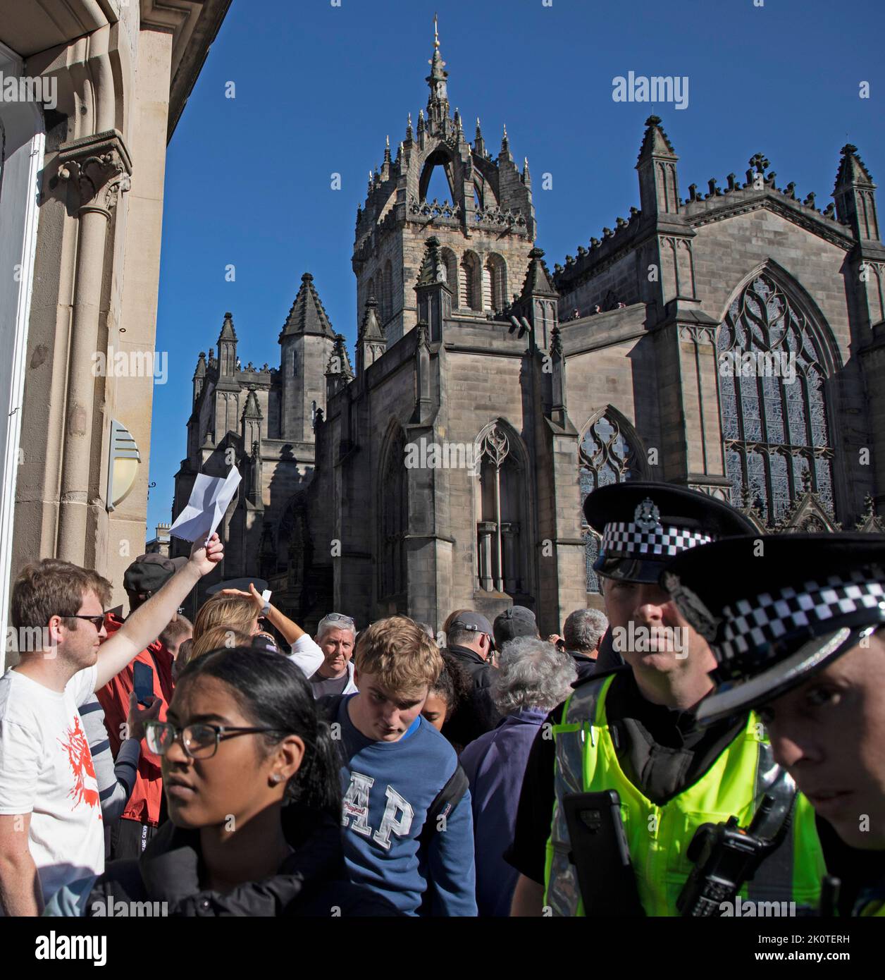 Royal Mile, Edinburgh, Scotland, UK. Crowds gather for Coffin of Her Majesty Queen Elizabeth II departing St Giles Cathedral. 13th September 2022. Pictured: One young man holds up a piece of paper as a protest, believed to be blank as police officers and pedestrians pass. Credit: Arch White/alamy live news. Stock Photo