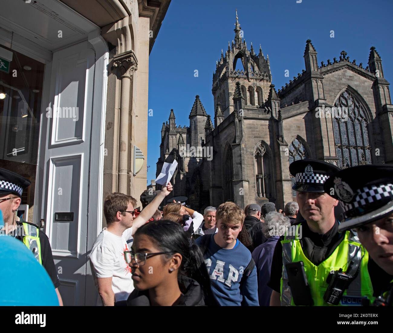 Royal Mile, Edinburgh, Scotland, UK. Crowds gather for Coffin of Her Majesty Queen Elizabeth II departing St Giles Cathedral. 13th September 2022. Pictured: One young man holds up a piece of paper as a protest, believed to be blank as police officers and pedestrians pass. Credit: Arch White/alamy live news. Stock Photo
