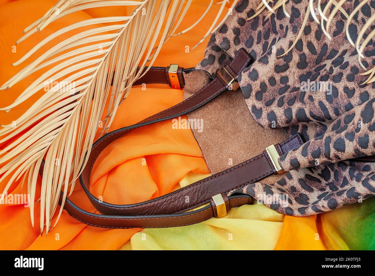 Handbag embossed under exotic skin of animal against background of bright stoles and tropical palm. Accessories concept Stock Photo