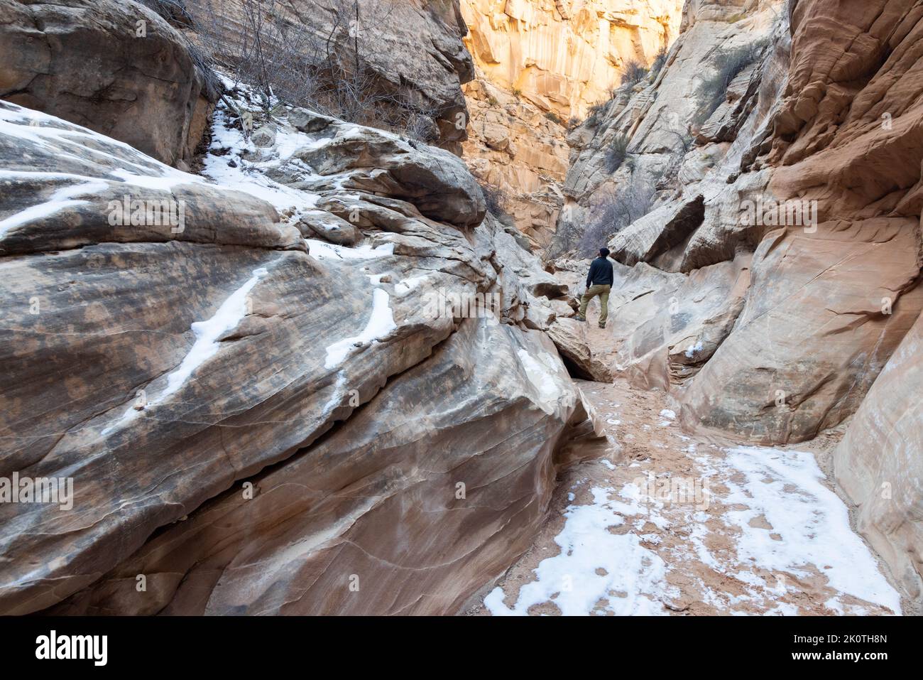 A male hiker pausing to admire the dynamic canyon walls of the Cottonwood Narrows as snow clings to the ground. Grand Staircase-Escalante National Mon Stock Photo