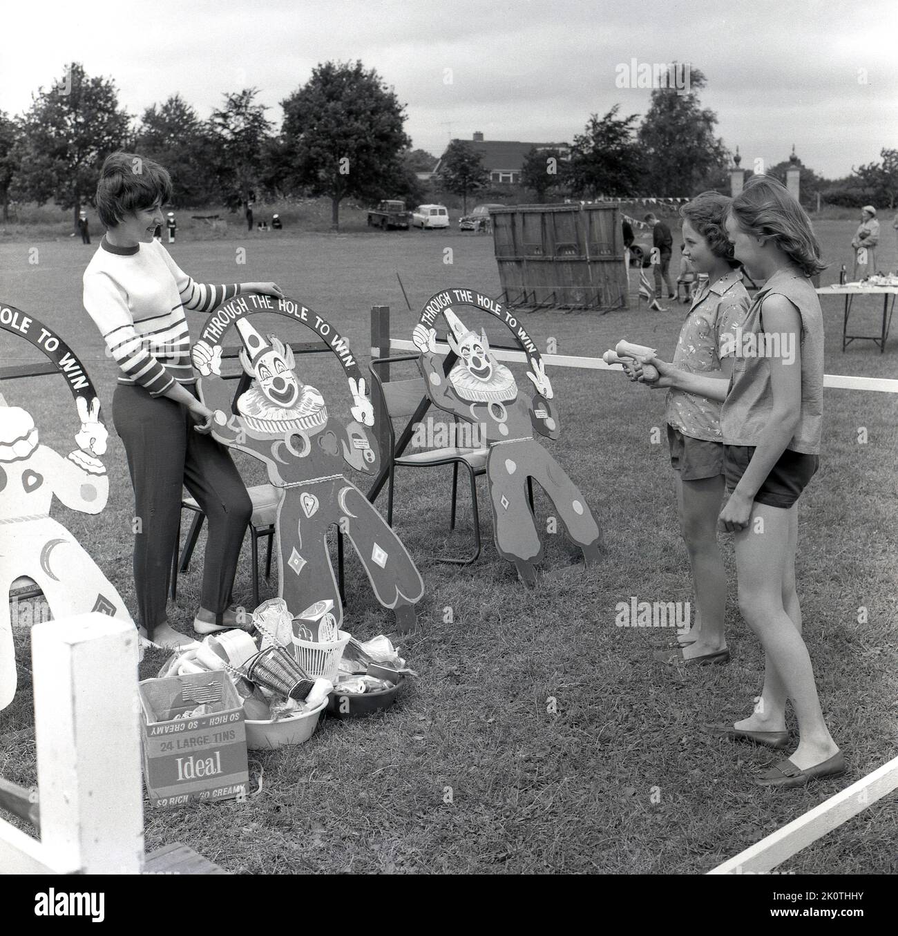 1964, historical, English village fete, outside in a field two girls playing a game, 'Through The Hole To Win', Stone, Buckinghamshire, England, UK. Stock Photo