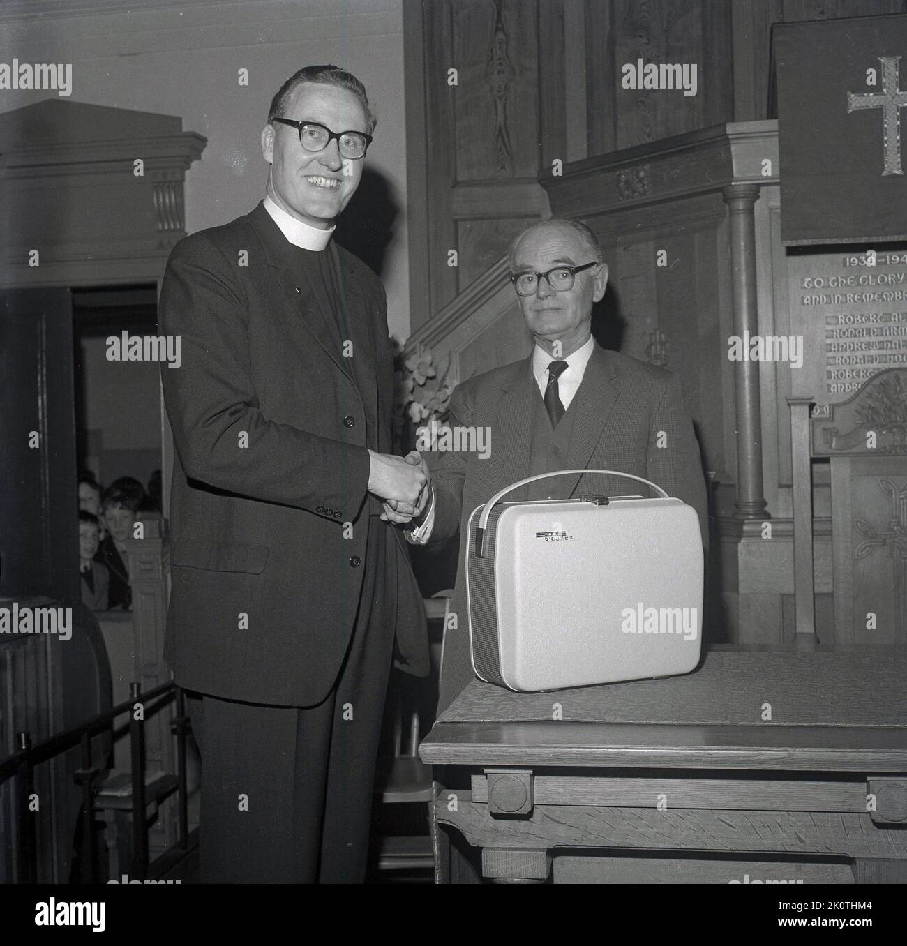 1965, historical, inside a church, a vicar or minister shaking the hands of an elderly church warden and presenting him with a gift, a portable tape recorder, St Andrews, Fife, Scotland, UK. Stock Photo