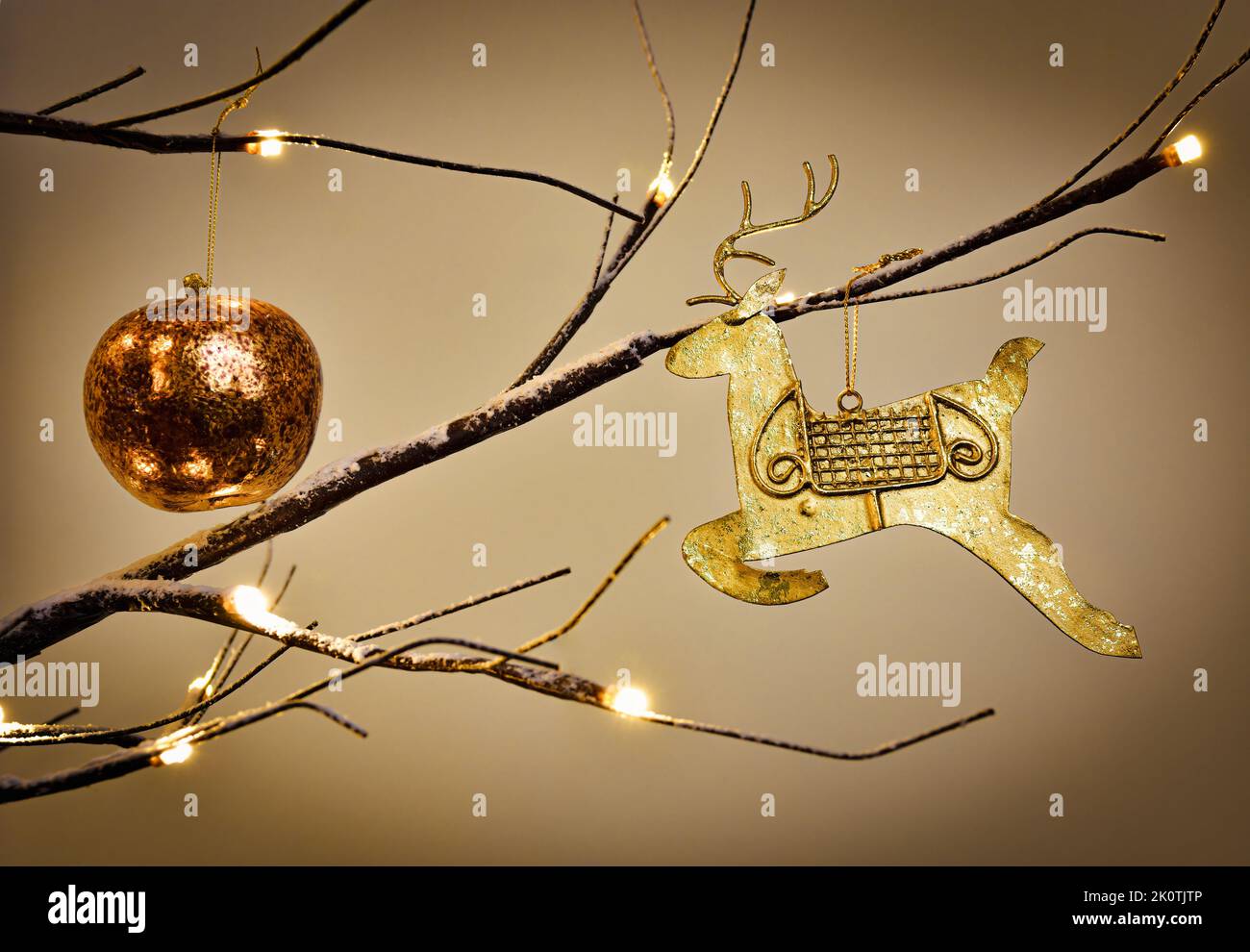 Gold reindeer decoration hanging from a modern Twig Tree Christmas Tree Decorated in traditional gold Stock Photo