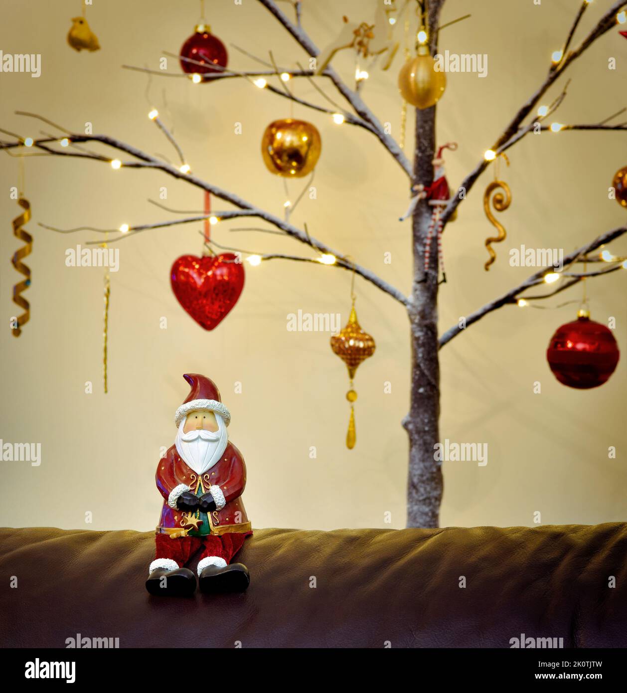 Father Christmas figure sat in front of a Twig Tree Christmas Tree Decorated in traditional red and gold Stock Photo