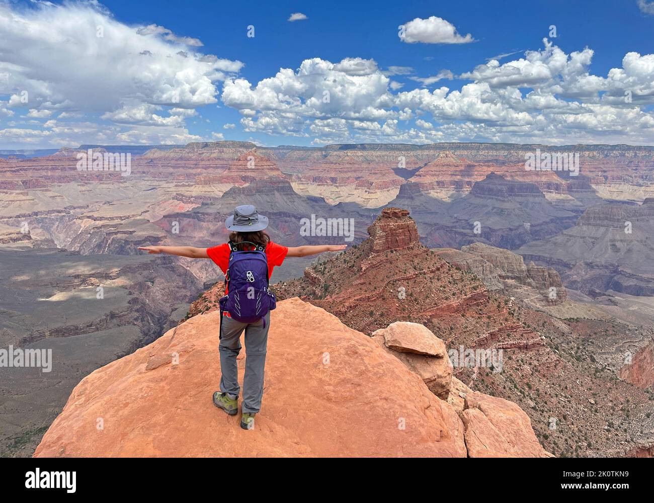 Aerial panoramic view of South Kaibab Trail in Grand Canyon with young girl tourist standing up with open arms on the rock, Arizona, USA Stock Photo