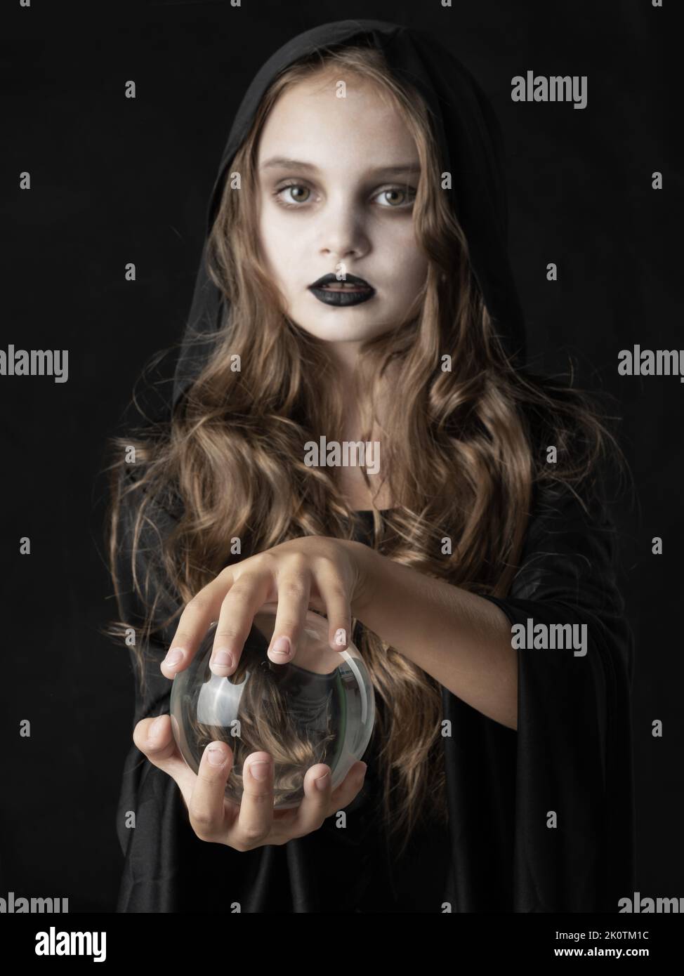 Little girl in Halloween witch costume and dark make-up holding crystal ball isolated on black background Stock Photo