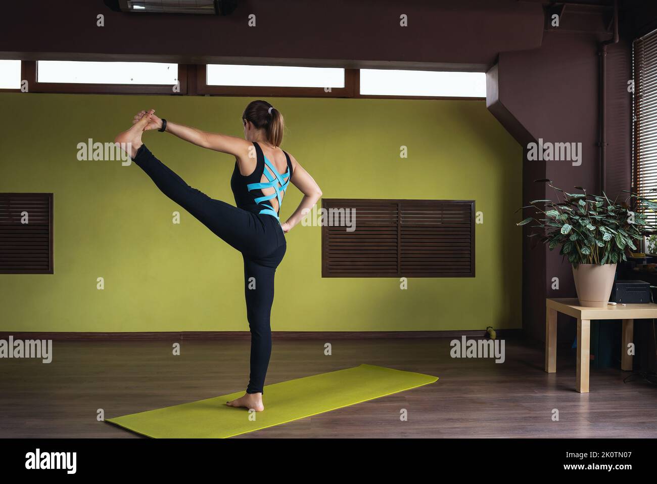 Woman in sports overalls practicing yoga doing Utthita hasta padangushthasana exercise, outstretched leg pose, training while standing on mat in studi Stock Photo